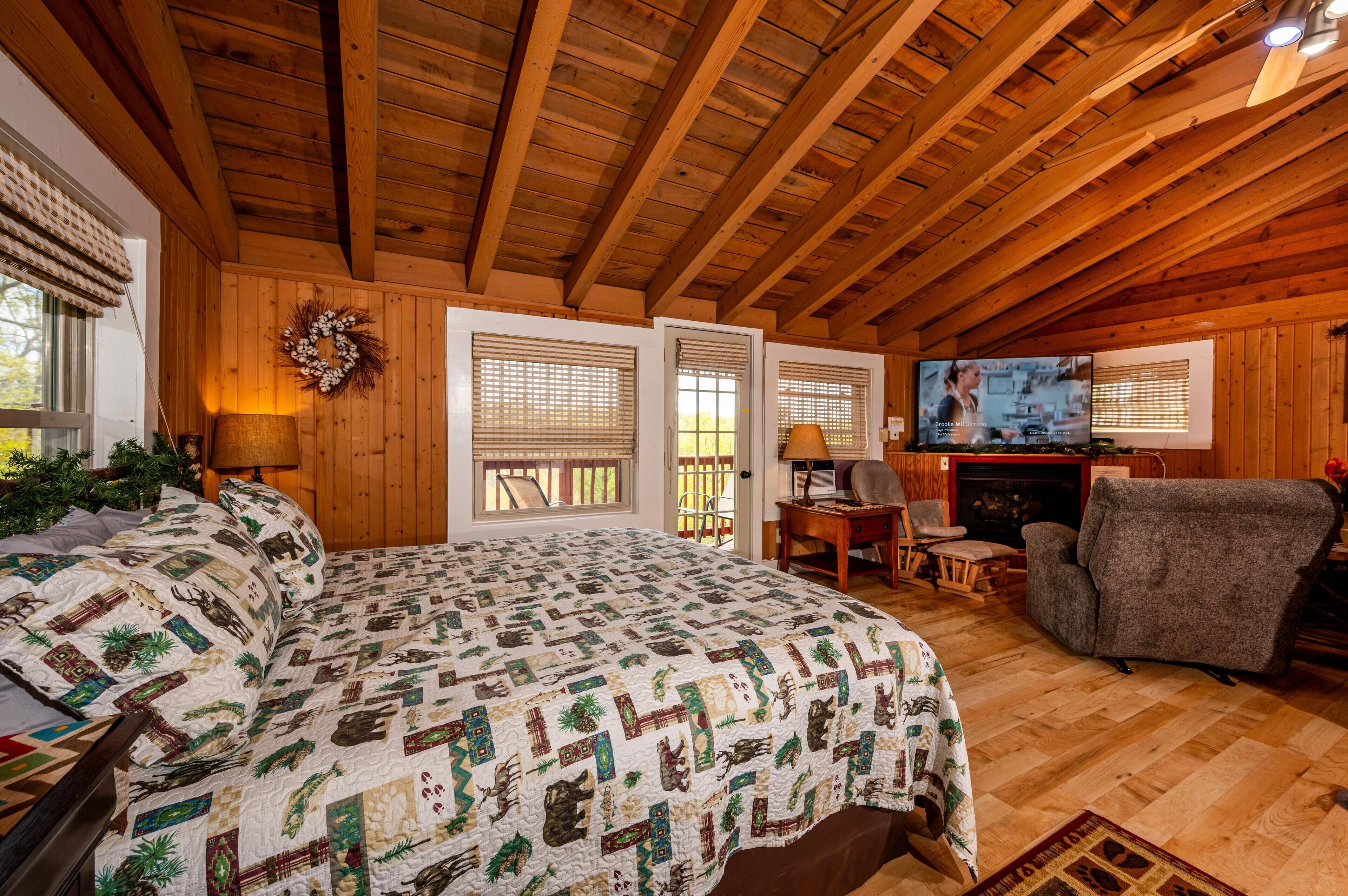A cozy cabin with a wooden ceiling, a large bed with a patterned quilt, a television, and a fireplace.