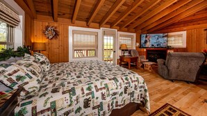 A cozy cabin with a wooden ceiling, a large bed with a patterned quilt, a television, and a fireplace. - Mountain View Log Cabin | Hot Tub, 3 Kings & Game Room 3BR, 3BA (Nashville)