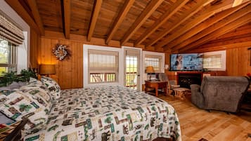 A cozy cabin with a wooden ceiling, a large bed with a patterned quilt, a television, and a fireplace.