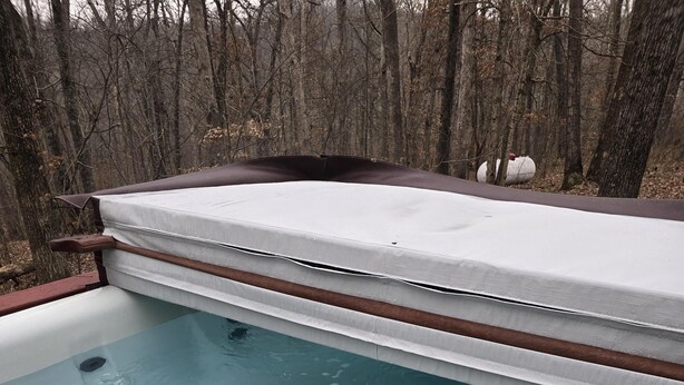 Un bain à remous doté d’un bord en bois et d’une structure métallique, entouré d’une zone boisée.