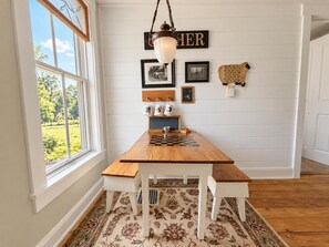 A dining area with a wooden table, benches, a chandelier, and a view of a garden through a window. - Farmhouse Retreat 2 Miles to Nashville | Hot Tub 3BR, 2BA (Nashville)