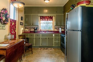 A kitchen with green cabinets, a refrigerator, a sink, and a window with floral curtains. - Farmhouse Retreat 2 Miles to Nashville | Hot Tub 3BR, 2BA (Nashville)
