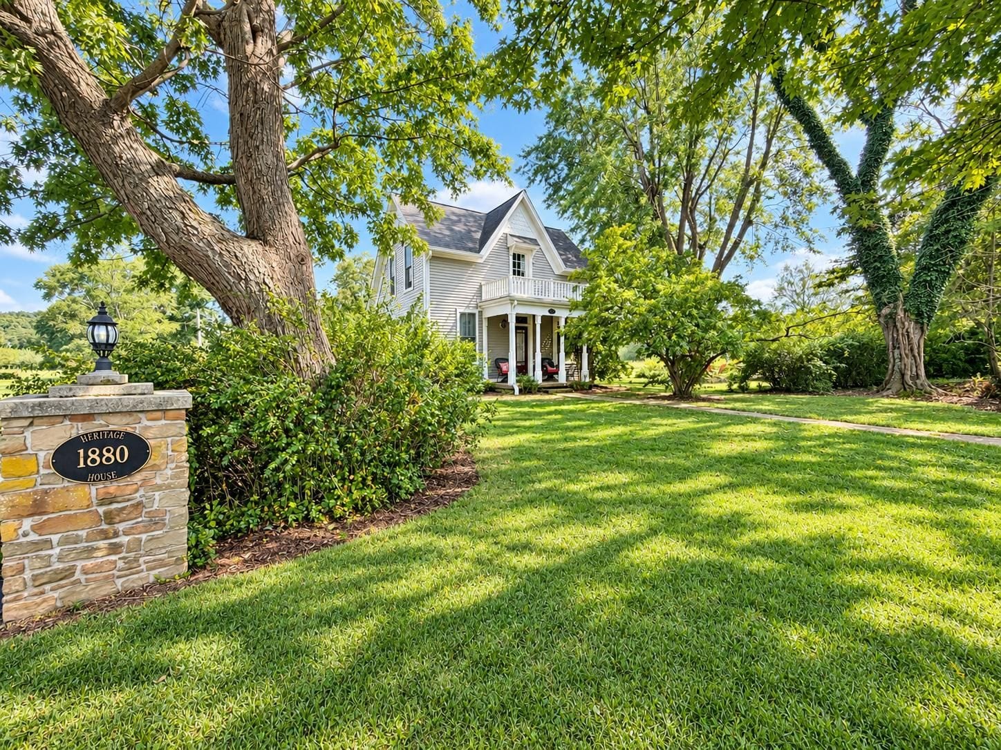 A heritage house with a stone sign, a well-maintained lawn, and mature trees.