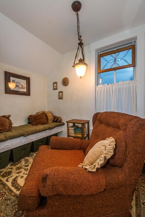 A cozy living room with a brown sofa, a bench, and a small table. There is a wall-mounted light fixture above the sofa and a window with a curtain. - Farmhouse Retreat 2 Miles to Nashville | Hot Tub 3BR, 2BA (Nashville)