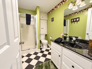A bathroom with a checkered floor, a shower, a toilet, and a vanity with a mirror. - Farmhouse Retreat 2 Miles to Nashville | Hot Tub 3BR, 2BA (Nashville)