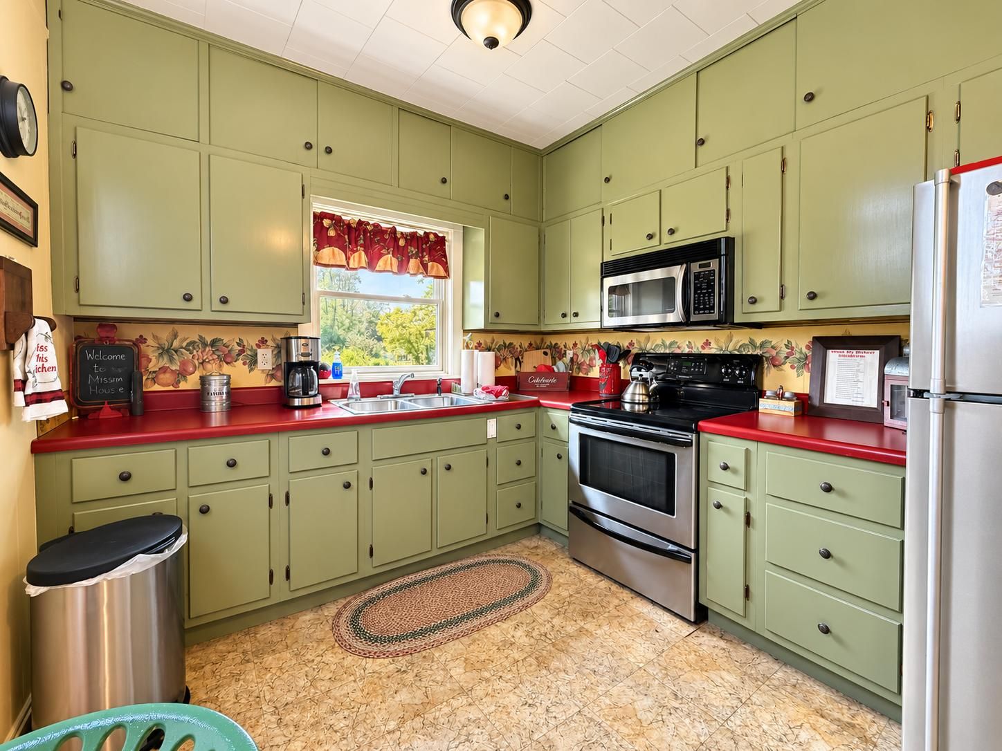 Een keuken met groene kasten, een rode aanrecht, een roestvrijstalen spoelbak, een magnetron, een oven en een koelkast.