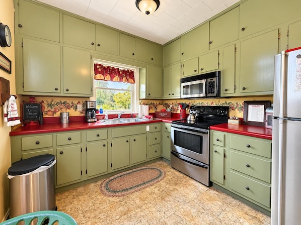 A kitchen with green cabinets, a red countertop, a stainless steel sink, a microwave, an oven, and a refrigerator.