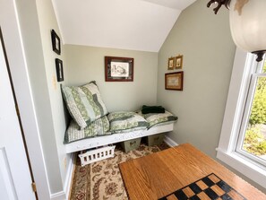 A cozy reading nook with a cushioned bench, a wooden table, and a window with a view of greenery. - Farmhouse Retreat 2 Miles to Nashville | Hot Tub 3BR, 2BA (Nashville)