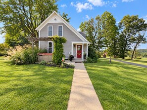 A two-story house with a red front door, a covered porch, and a well-maintained lawn. - Farmhouse Retreat 2 Miles to Nashville | Hot Tub 3BR, 2BA (Nashville)