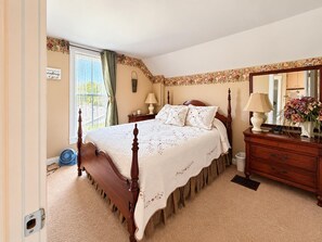 A bedroom with a four-poster bed, a dresser, a mirror, and a window with curtains.
