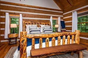A log cabin bedroom with a wooden bed frame, two bedside tables, and a bench.