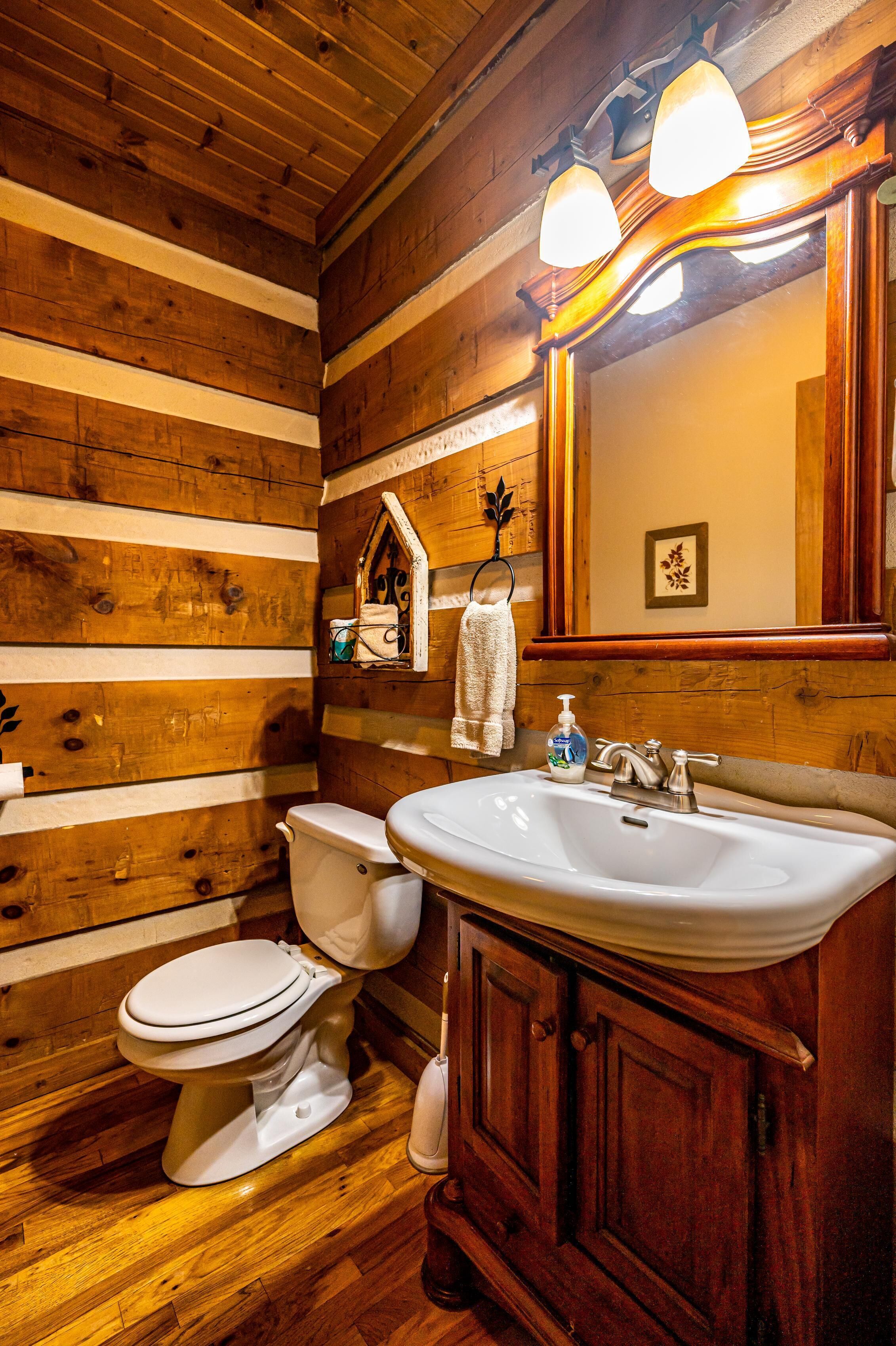 A wooden-paneled bathroom with a toilet, sink, and mirror.