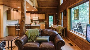 Interior acolhedor de uma cabana, com área de jantar, cozinha e uma grande janela com vista para o exterior.