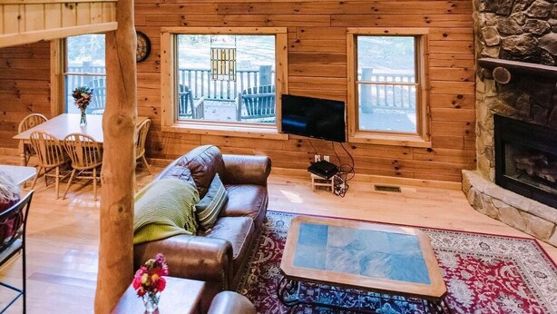 Interior de uma cabana de madeira com um quarto no loft, lareira de pedra e janelas amplas.