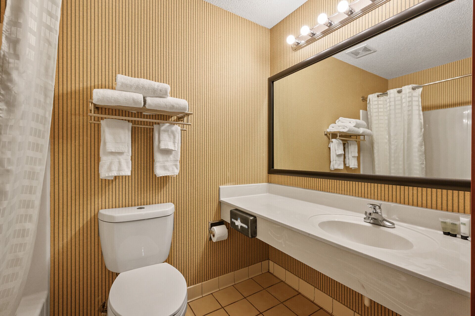 A bathroom with a toilet, sink, and mirror. There are towels hanging on a rack and a shower curtain.