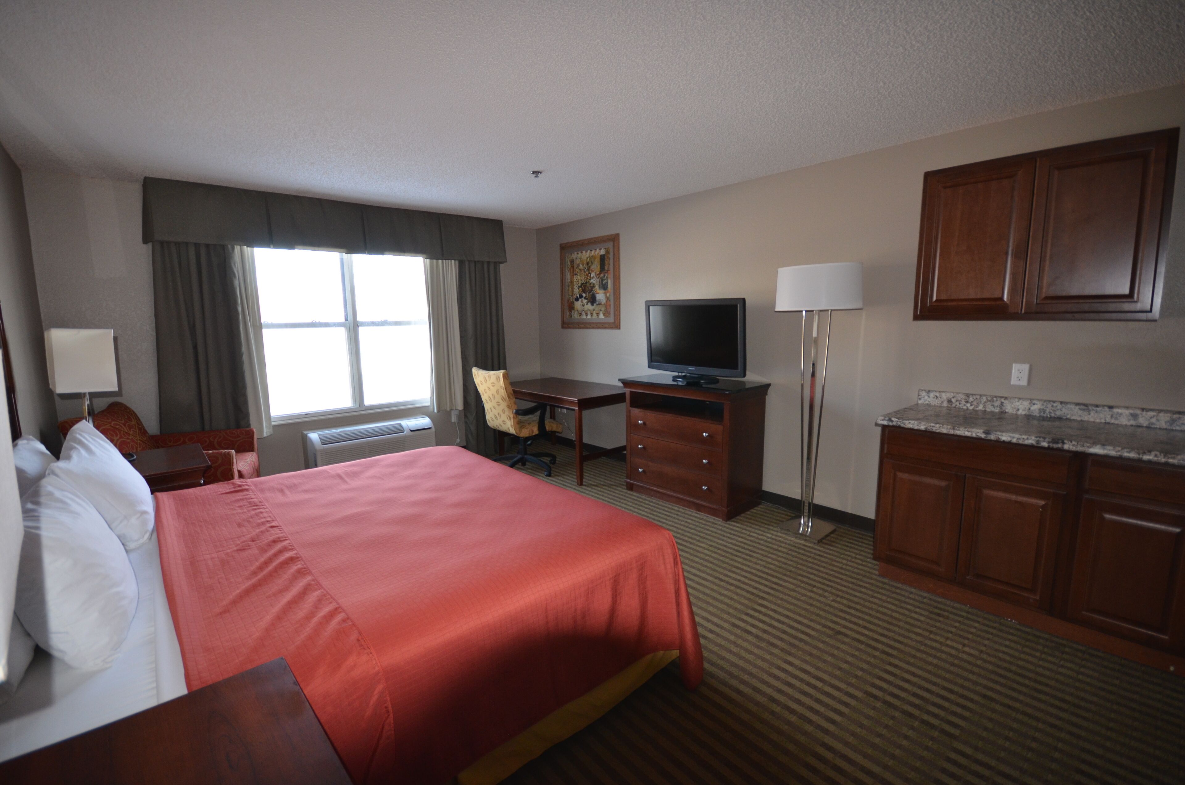 Een hotelkamer met een groot bed, een bureau, een televisie, een stoel en houten kasten.