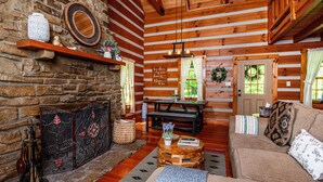 L’intérieur d’un chalet confortable, avec des murs en rondins de bois, une cheminée en pierre, des étagères en bois, un canapé et une table à manger.