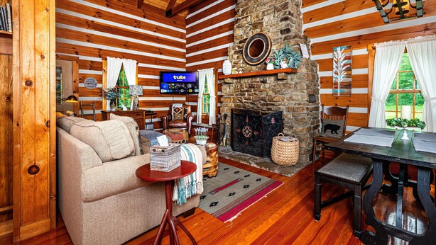 L’intérieur d’un chalet confortable, avec une cheminée en pierre, des murs en bois, un téléviseur et un coin repas.