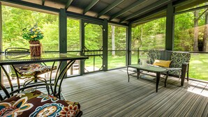 Un espace extérieur abrité, équipé d’une table et de chaises, d’un banc rembourré, et offrant une vue sur un paysage verdoyant et luxuriant.