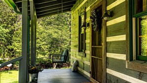 Une cabane en bois avec une véranda, un banc et un pot de fleurs.