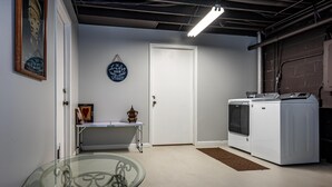 A laundry room with a washing machine, a table with a vase, and a glass table with a metal frame. - Cabin w/ Pond, Hot Tub & Pool Table | Family-Friendly Retreat 3BR, 2BA (Nashville)