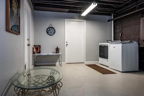 A laundry room with a washing machine, a table with a vase, and a glass table with a metal frame. - Cabin w/ Pond, Hot Tub & Pool Table | Family-Friendly Retreat 3BR, 2BA (Nashville)