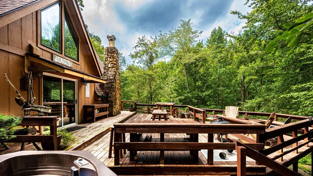 A wooden deck with outdoor seating and a hot tub. - Cabin w/ Pond, Hot Tub & Pool Table | Family-Friendly Retreat 3BR, 2BA (Nashville)