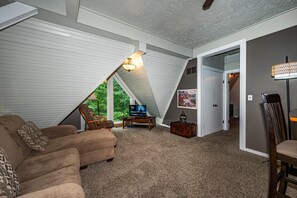 A cozy living room with a sloped ceiling, a television, a wooden coffee table, and a brown sofa. - Cabin w/ Pond, Hot Tub & Pool Table | Family-Friendly Retreat 3BR, 2BA (Nashville)