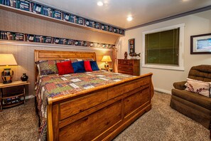 Une chambre à coucher avec un lit en bois, une bibliothèque, une fenêtre avec des stores et une chaise.