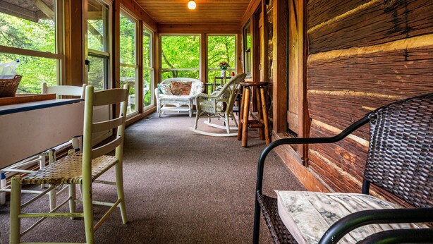 A covered porch with wicker furniture, large windows, and a wooden interior. - 2 BA, (1 is a loft), 1 BA Log Cabin (Morgantown)