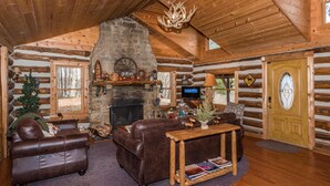 A log cabin interior with a fireplace, leather furniture, and a wooden ceiling. - Secluded 100-Acre Cabin | Hot Tub, Views & Wildlife 3BR, 1.5BA (Nashville)