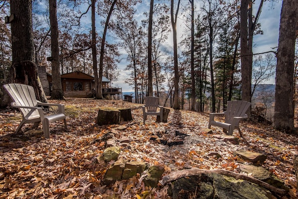 Une cabane avec un foyer et des fauteuils Adirondack, située dans un cadre forestier.