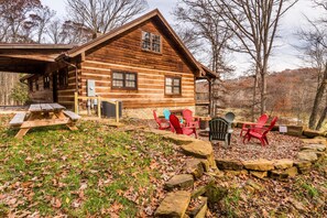 A rustic log cabin with a covered porch, a picnic table, and outdoor seating.