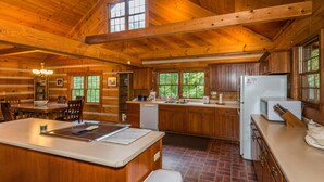 A wooden cabin interior with a kitchen, dining area, and a large window. - Large Log Cabin | Hot Tub, Game Room & Near Nashville 5BR, 3BA (Nashville)