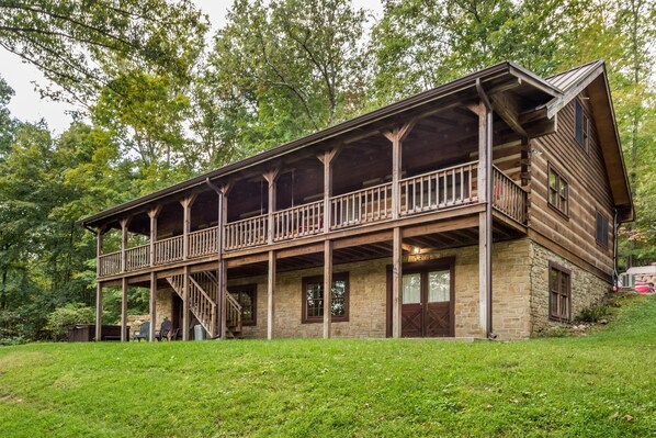A rustic log cabin with a balcony, stone foundation, and a staircase leading to the upper level.