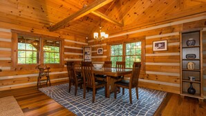 A wooden cabin interior with a dining table, chairs, and a chandelier. - Large Log Cabin | Hot Tub, Game Room & Near Nashville 5BR, 3BA (Nashville)
