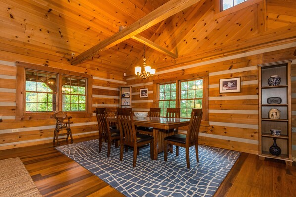 Interior de una cabaña de madera con una mesa de comedor, sillas y un candelabro.