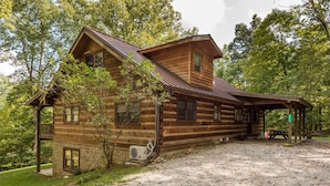 A log cabin with a stone foundation, a covered porch, and a gravel driveway. - Large Log Cabin | Hot Tub, Game Room & Near Nashville 5BR, 3BA (Nashville)