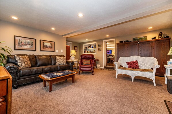 A living room with a brown leather sofa, a white wicker sofa, a wooden coffee table, and a red leather armchair. - Ridgetop Cabin w/ Hot Tub & Sunset Views | 2 Min to Nashville 2BR+, 2 BA (Nashville)