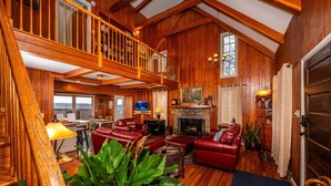 A spacious living area with a fireplace, red leather sofas, a wooden staircase, and a dining area. - Ridgetop Cabin w/ Hot Tub & Sunset Views | 2 Min to Nashville 2BR+, 2 BA (Nashville)