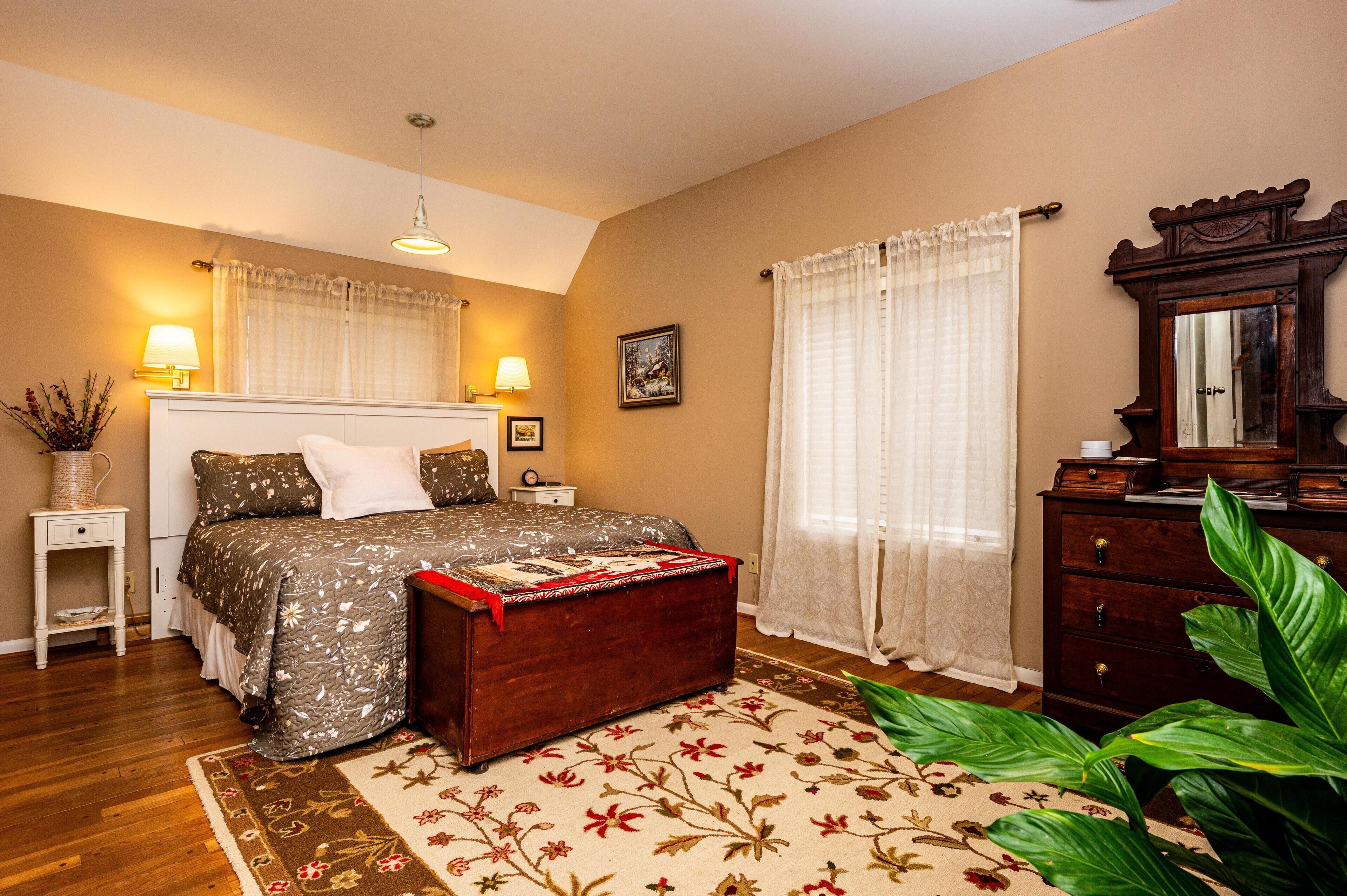 A bedroom with a bed, bedside tables, a dresser, a mirror, and a large plant.