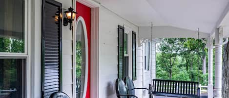 A porch with three black chairs, a red door, and a white exterior wall.