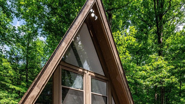 Eine Holz-A-Rahmen-Hütte mit großen Fenstern und einer Terrasse mit Adirondack-Stühlen.