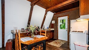 Eine Küche mit Holzbalken, einem Esstisch mit Blumenvase und einem weißen Kühlschrank.