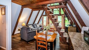 Ein gemütliches Schlafzimmer im Dachgeschoss mit Holzbalkendecke, einem Esstisch mit Stühlen, einer Couch und einem Fernseher.