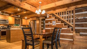 A wooden interior with a dining table, chairs, a kitchen area, and a staircase. - Ridge View Log Cabin | Hot Tub, Game Shed & EV Charger 2BR, 2 BA (Nashville)