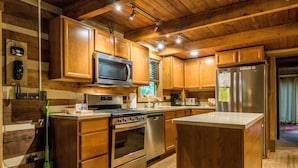 A modern kitchen with wooden cabinets, stainless steel appliances, and a central island. - Ridge View Log Cabin | Hot Tub, Game Shed & EV Charger 2BR, 2 BA (Nashville)