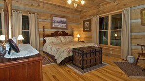 Una habitación acogedora de madera con una cama grande, un cofre de madera y un escritorio con lámparas.