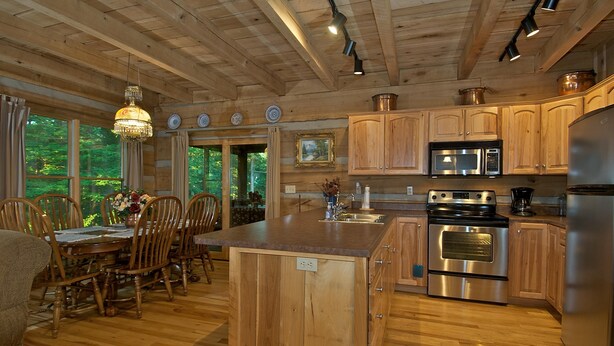 Una cocina de madera con una isla central, electrodomésticos de acero inoxidable y un comedor con sillas y mesa de madera.