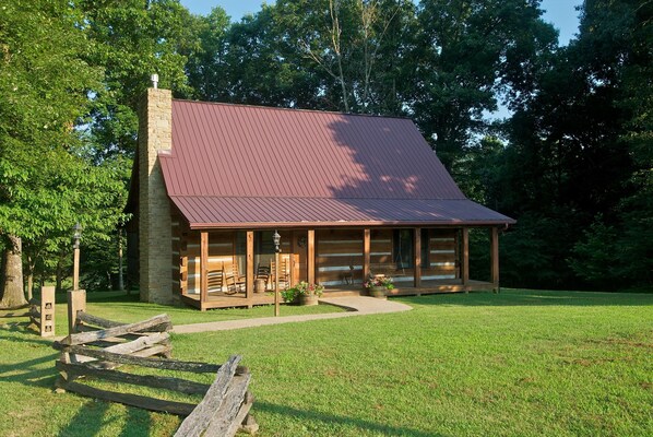 A log cabin with a sloped roof, a stone chimney, and a porch with outdoor seating. - Log Cabin Near Nashville | Hot Tub, Screened Porch & Game Loft2BR, 2BA (Nashville)